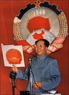 a man standing in front of a microphone and holding up a piece of paper with an emblem on it