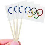 hand holding four olympic stick flags in front of the olympics logo on a white background