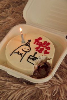 a birthday cake in a plastic container with a lit candle