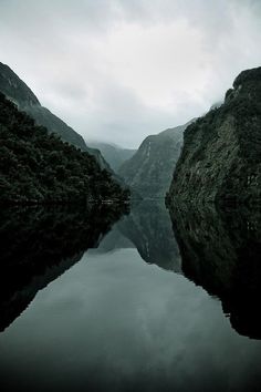 a body of water surrounded by mountains under a cloudy sky