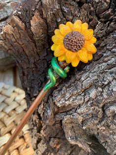 a yellow sunflower sitting on top of a wooden stick next to a tree trunk