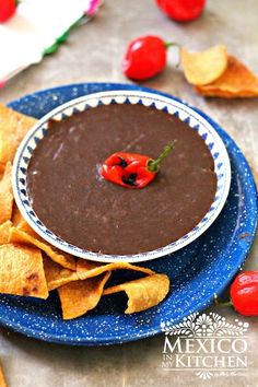 a blue plate topped with a chocolate dip surrounded by tortilla chips and peppers