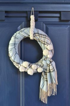 a wreath with pom poms hanging on a blue door frame, decorated with white flowers and tassels