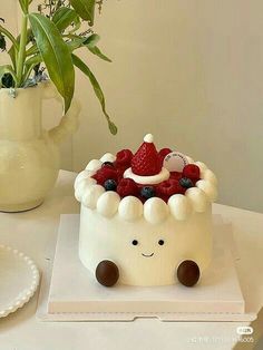 a white cake with berries and cream on top sitting next to a potted plant