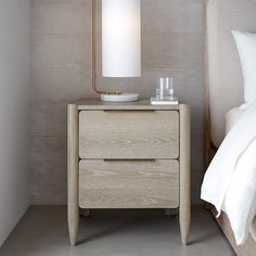 a night stand with a lamp on it next to a bed