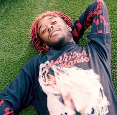 a man with dreadlocks laying on the ground wearing a black shirt and red pants