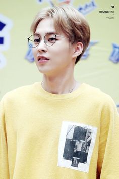 a young man with glasses standing in front of a wall