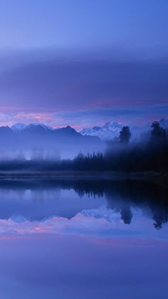 a lake with mountains in the background and fog hanging over it's surface at dusk