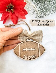 a hand holding a football ornament with the name jackson on it and a poinsetti in the background