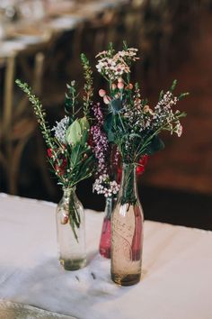 two vases filled with flowers sitting on top of a white tablecloth covered table