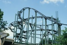 a roller coaster going down the side of a hill with trees in the foreground