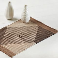 two white vases sitting next to each other on a wooden table with a brown and tan rug