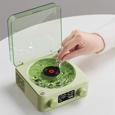 a person is pressing the button on a green record player that's sitting on a white table