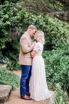 a man and woman standing next to each other in front of some bushes with trees