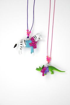 two necklaces with zebra and dinosaur charms hanging from strings on a white background,