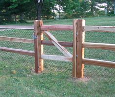 a wooden fence in the middle of a grassy area with trees and grass behind it