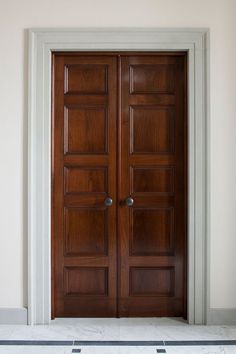 two wooden doors in an empty room with tile flooring and white trim on the walls