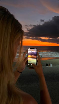 a woman taking a photo with her cell phone on the beach at sunset or dawn