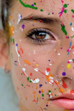 a woman with multicolored paint all over her face and cheek, looking at the camera