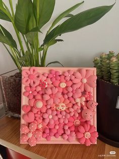 a pink frame with buttons and flowers in the shape of animals is sitting on a table next to a potted plant