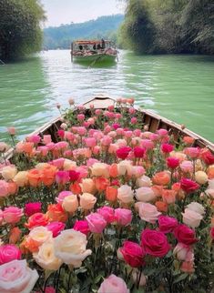 a boat filled with lots of pink and white flowers floating down a river surrounded by greenery