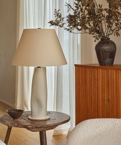 a table with a lamp on it next to a vase filled with flowers and a bowl