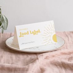 a white plate topped with a card next to a potted plant on top of a table