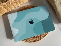 an apple laptop sitting on top of a table next to a wicker basket and pillow