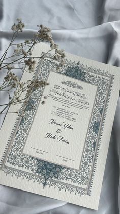 an ornate wedding card with blue and white designs on it, next to some dried flowers