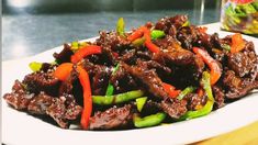 a white plate topped with beef and peppers next to a jar of pickles on a table