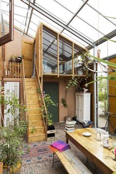 a table and benches in a room with plants on the walls, windows, and stairs