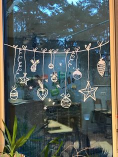 a window decorated with christmas decorations and ornaments hanging from it's side, next to a potted plant