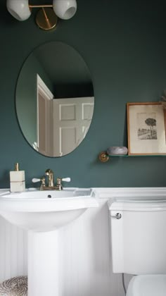 a white toilet sitting next to a bathroom sink under a round mirror on a wall