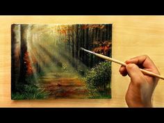 a person is holding a paintbrush in front of a painting on a wooden surface