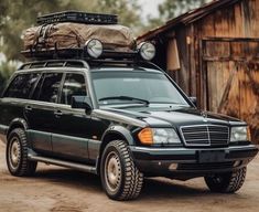 a mercedes benz wagon parked in front of a wooden building with luggage on the roof