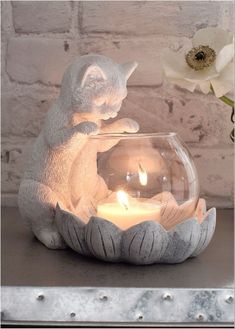 a cat figurine sitting on top of a table next to a lit candle