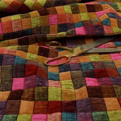 a pair of scissors sitting on top of a multicolored blanket next to a pair of shears