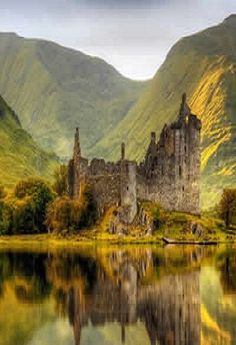 an old castle sitting on top of a mountain next to a lake in front of mountains