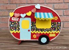 a red and yellow camper is sitting on a wooden table next to a brick wall