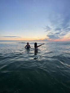 two people in the water at sunset with one holding her arms out to the side