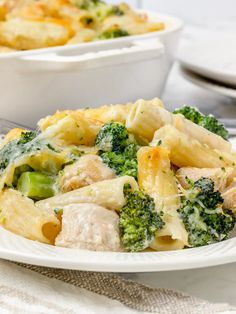 a white plate topped with chicken and broccoli covered in cheese sauce next to a bowl of pasta