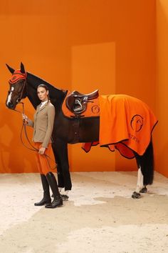 a woman standing next to a horse wearing an orange blanket