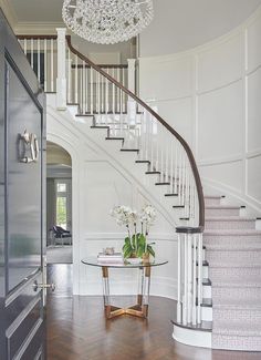 a white staircase with chandelier and glass table in the center, surrounded by wood flooring