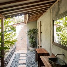 an outdoor bathroom with stone flooring and plants in the shower area, along with a wooden bench