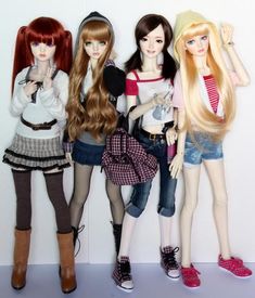 three dolls standing next to each other in front of a white wall and one is holding her hand up