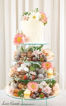 a three tiered cake with flowers on the top is surrounded by cupcakes and macaroons