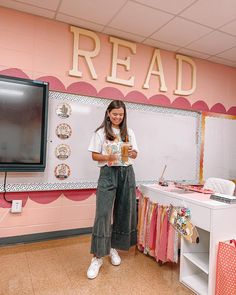 a girl standing in front of a desk holding a cup