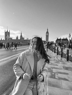 a woman is walking down the street with her hand in her pocket and wearing a coat