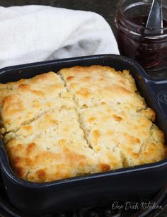 a pan filled with bread next to a jar of jam on top of a table