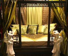 a canopy bed with two statues on each side and green drapes over the top